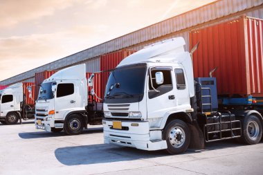 Deponun otoparkındaki yarı karavan kamyonları. Rıhtım deposunda yük kamyonu var. Dağıtım Deposu Merkezi. Konteynır nakliyesi. Nakliye Aracı Lojistiği, Kargo Taşımacılığı.