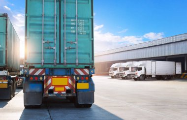 Deponun otoparkındaki yarı karavan kamyonları. Rıhtım deposunda yük kamyonu var. Dağıtım Deposu Merkezi. Nakliye konteynırı. Nakliye Aracı Lojistiği, Kargo Taşımacılığı.