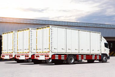 Depo 'daki otoparkta beyaz kamyonlar. Kargo konteynırı. Rıhtım deposunda yük kamyonu var. Dağıtım Deposu. Kamyon nakliyesi. Nakliye Aracı Taşımacılığı.