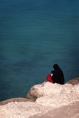 Muslim woman with hijab. she is sitting on the stone beach. The 