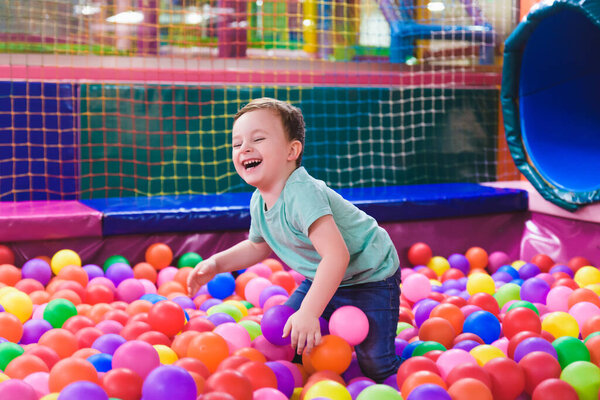 Happy laughing child laughing in an indoor play center. Children playing with colored balls in the playground ball pool. Party.
