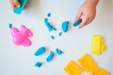 Küçük çocuk elleri, beyaz arka planda mavi manken kiliyle oynarken yakınlaşıyor. Kil ile ev eğitimi oyunu. Üst Manzara. Erken kalkınma kavramı.