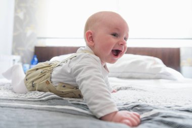 Beyaz güneşli yatak odasında bebek bezi takan bir çocuk. Yeni doğmuş çocuk yatakta dinleniyor. Çocuklar için çocuk odası. Çocuklar için tekstil ve yatak. Aile sabahı evde..