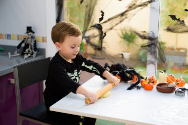 Evde cadılar bayramı kurabiyesi yapmak için iskelet yoğurma unu gibi giyinmiş bir çocuk. Cadılar Bayramı hazırlanıyor.