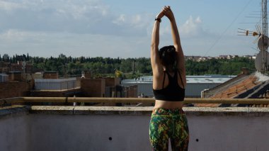 Yazın terasta esneme egzersizi yapan genç bir kadın.