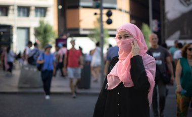 Arka planda insanlar olan genç peçeli Müslüman kadın caddenin ortasında.