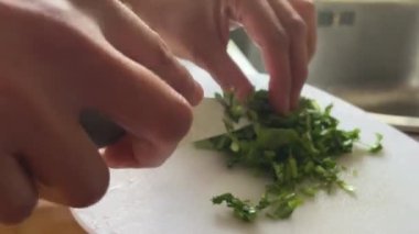 Birisi kesme tahtasıyla maydanoz kesiyor. Maydanoz küçük parçalara ayrılıyor.