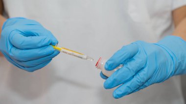 Mavi eldiven giyen biri termometre ve şırınga tutuyor. Kişi ateş etmeye hazırlanıyor.