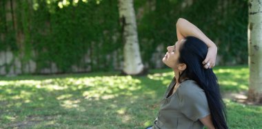 Bir kadın çimenlerde oturuyor ve gökyüzüne bakıyor. Gülümsüyor ve anın tadını çıkarıyor.