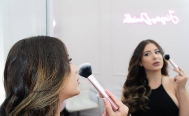 Bir kadın neon tabelanın önünde makyaj yapmaya hazırlanıyor. 