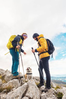 Sırt çantaları ve yürüyüş direkleriyle donatılmış bir çift yürüyüşçü köpekleriyle yüksek dağ rotası çiziyor. Dağcılar evcil hayvanlarıyla bir dağ zirvesine tırmanıyorlar. açık hava aktiviteleri.