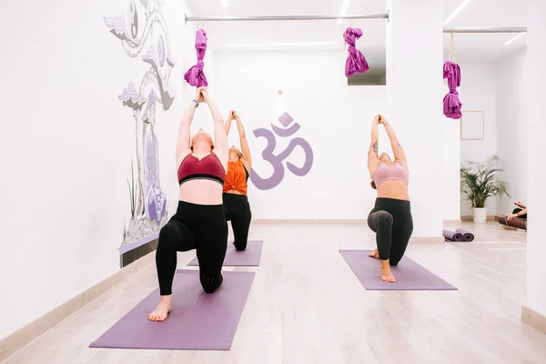 three women practicing warrior pose (yoga exercise) on their mats in a yoga studio. Yoga classes. exercise and healthy life. \
