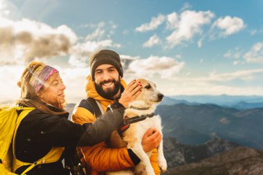 Bir çift yürüyüşçü köpekleriyle dağ rotası çiziyor. Dağcı, arka planda dağ manzarası olan köpeğini kollarında tutuyor. Kadın evcil köpek.
