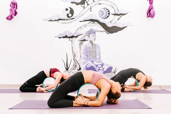 背景に仏画を描いたスタジオでヨガホイールを使ってヨガの練習をしている3人の女性 健康的なライフスタイルと運動 — ストック写真