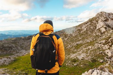 Sırt çantalı, kalın elbiseli, sarı dağ ceketli, tırmanacağı dağ zirvesini izleyen bir adam. dağ zirvelerine tırmanmak