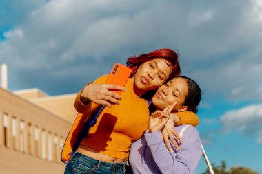İki genç Latin kız, arkadaşlar ve kız kardeşler okul çıkışında akıllı bir telefonla selfie çekiyorlar. İki Latin genç cep telefonu kullanıyor..
