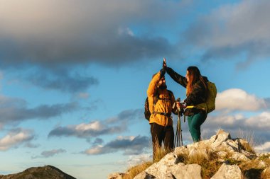 Couple of mountaineering hikers, with backpack and trekking poles, high-fiving as they reach the top of a mountain. Outdoor sports and weekend activities.