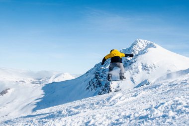 Sarı elbiseli, kar kayağı antrenmanı yapan ve güneşli bir günde karda zıplayan tanınmamış biri. kış ve dağ sporları