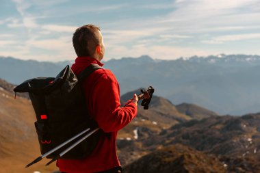 Kırmızı elbiseli dağcı, sırt çantası ve yürüyüş direkleri ile bir mola verir ve yüksek dağ yürüyüşü sırasında manzarayı inceler. spor ve macera