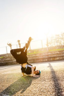 Güneş batarken basketbol sahasında dans eden mavi saçlı beyaz bir çocuk. egzersiz ve gençlik kültürü. Sokak dansçısı ve hip-hop kültürü.
