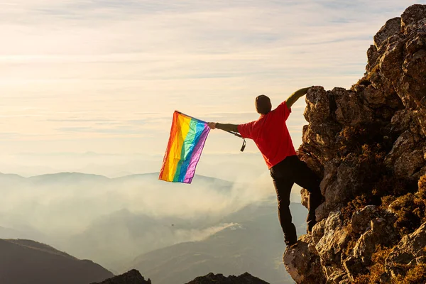 Hegymászó Ember Csúcsot Rendez Egy Hegyen Szivárvány Zászlót Lengetve Naplementekor — Stock Fotó