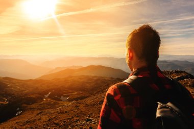 Dağlarda yürüyüş yaptığı bir gün boyunca dağlarda gün batımını seyreden dağcı bir adamın arkasından. macera ve açık hava sporu. hafta sonu aktiviteleri