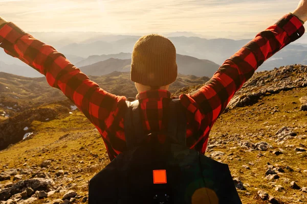 Sırt çantalı, yün şapkalı, dağlarda gün batımını seyreden bir yürüyüşçünün arkasından. Açık hava sporları ve macera