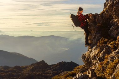 Kırmızı elbiseli ve sırt çantalı beyaz dağcı güvenlik önlemleri olmadan dağa tırmanıyor. Spor ve macera. Dağda risk.