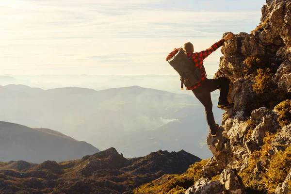 Sırt çantalı erkek yürüyüşçü gün batımında halatsız dağa tırmanıyor. Bir dağın zirvesinden gün batımını seyreden bir adam. spor ve macera.