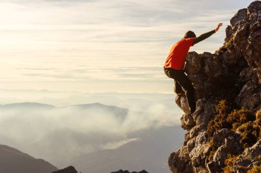 Kırmızı elbiseli bir erkek, dağın zirvesine ulaşmak için iple veya güvenlik önlemi olmadan kayaya tırmanıyor. Riskli spor. macera