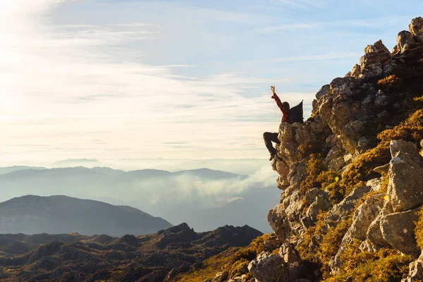 stock image unrecognizable hiker with backpack raises his arms in victory sitting on the peak of a mountain contemplating the sunset. sport and adventure