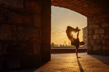 Gün batımında sokakta dans eden genç bir çocuğun arka ışıklandırılmış silueti. Gençlik kültürü ve hip hop. Sokak dansçısı.