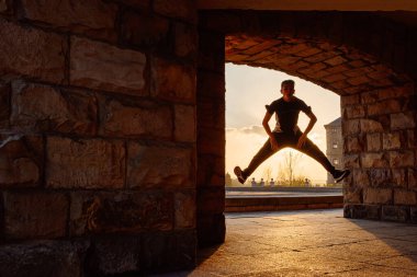 Gün batımında sokakta dans eden genç bir çocuğun arka ışıklandırılmış silueti. Gençlik kültürü ve hip hop. Sokak dansçısı.