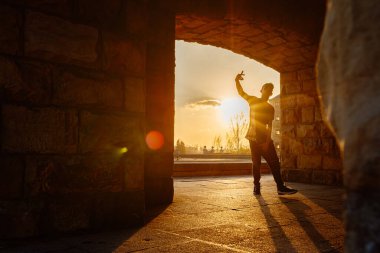 Gün batımında sokakta dans eden genç bir çocuğun arka ışıklandırılmış silueti. Gençlik kültürü ve hip hop. Sokak dansçısı.