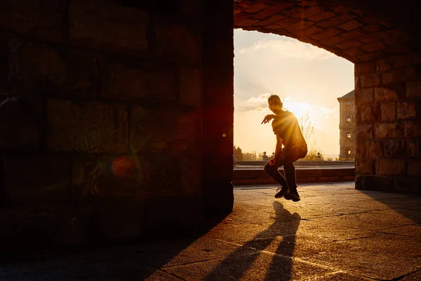 Gün batımında sokakta dans eden genç bir çocuğun arka ışıklandırılmış silueti. Gençlik kültürü ve hip hop. Sokak dansçısı.
