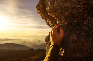 Gün batımında bir dağın kayasına tutunan bir dağcının ilk insan görüntüsü. Macera ve spor. risk sporu.