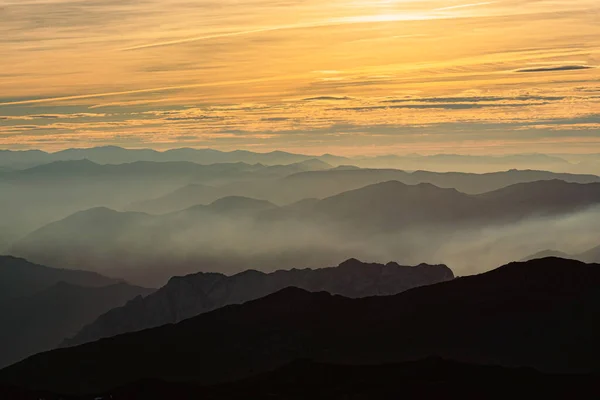 landscape photography of mountain silhouettes with mist and clouds at sunset.