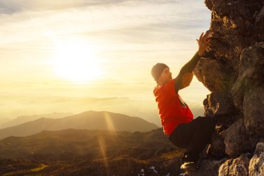 Yün şapkalı ve dövmeli beyaz adam gün batımında dağa tırmanıyor. ekstrem spor ve açık hava aktiviteleri.