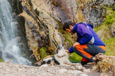 Beyaz adam şelalenin yakınındaki bir dağ yolunda köpeğiyle oynuyor. evcil hayvan sporu ve macera ile seyahat