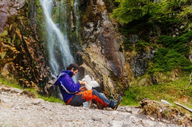 Beyaz adam şelalenin yakınındaki bir dağ yolunda köpeğiyle oynuyor. evcil hayvan sporu ve macera ile seyahat