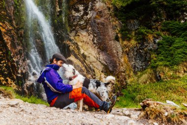 Beyaz adam şelalenin yakınındaki bir dağ yolunda köpeğiyle oynuyor. evcil hayvan sporu ve macera ile seyahat