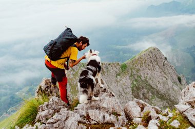 Dağcı adam dağın zirvesine ulaştıktan sonra köpeğine sarılıyor. Spor, yürüyüş ve macera..