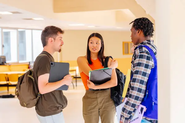 Multiracial group of college students with backpacks and school supplies chatting together in campus hallways. Education and diversity.