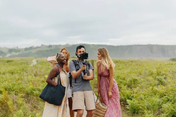 Male filmmaker with a group of female models reviewing the shots taken on the beach on his camera. Creative person at work