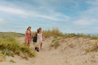 Plaj elbiseli üç arkadaşın yaz gezisi boyunca sahilde yürüdüğü çok ırklı bir grup.