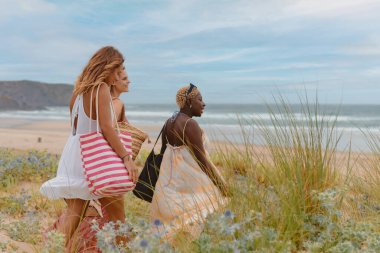 Plaj elbiseli üç arkadaşın yaz gezisi boyunca sahilde yürüdüğü çok ırklı bir grup.