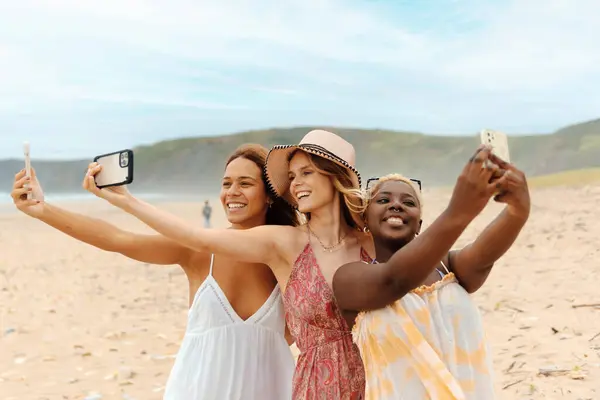 Sahilde üç arkadaşın yaz tatilinde sosyal ağlarda göstermek için akıllı telefonlarıyla fotoğraf çektikleri çok ırklı bir grup..