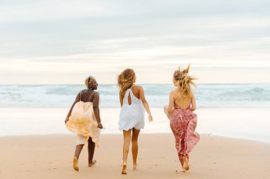 Sahilde denize doğru birlikte koşan üç genç bayandan oluşan çok ırklı bir grup. arkadaşlıklar ve yaz aktiviteleri