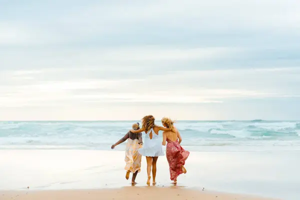 multiracial group of three young women of different races strolling along the beach looking out to sea. Friendship and unity. Summer trip.