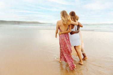 Farklı ten renkleri olan bir grup arkadaş deniz kıyısında birlikte yürüyorlar. Çok ırklı bir grup genç kadın. dostluk ve birlik.